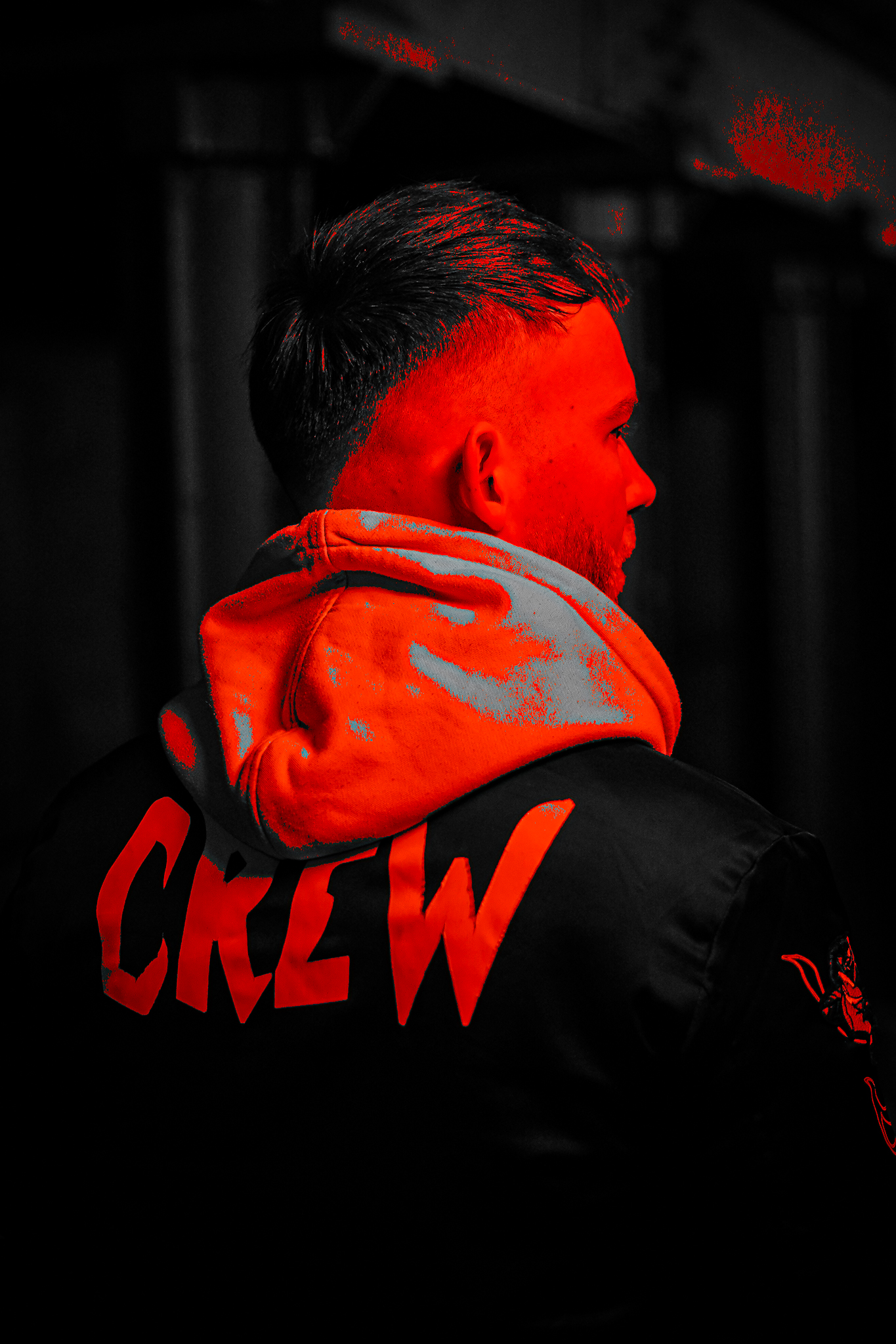 A man in a black jacket and hoodie with the word CREW on the back, lit with a red light. By NinoTurbaProductions