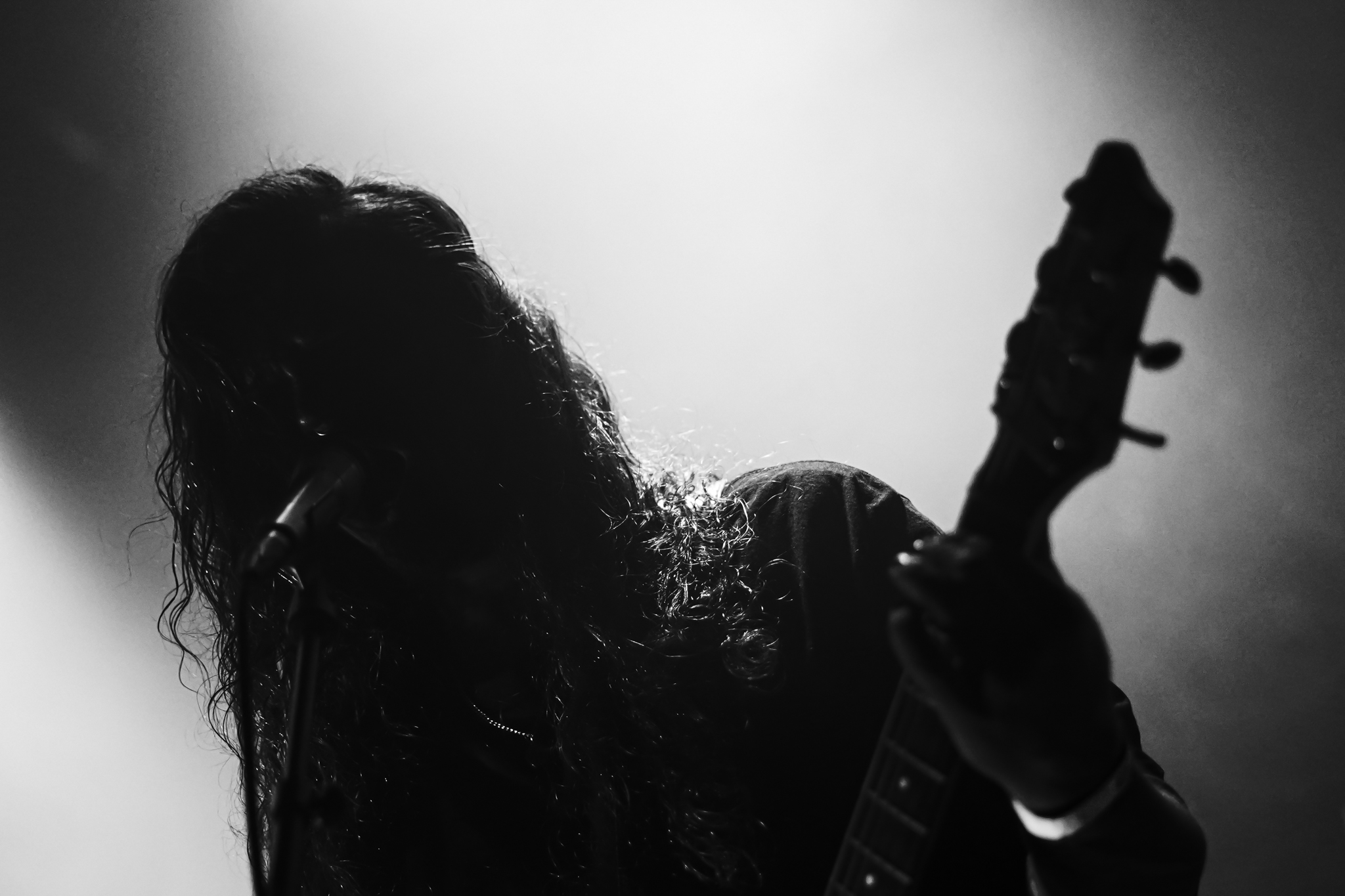 Silhouetted musician performs passionately on stage, singing into a microphone and playing guitar under dramatic lighting.