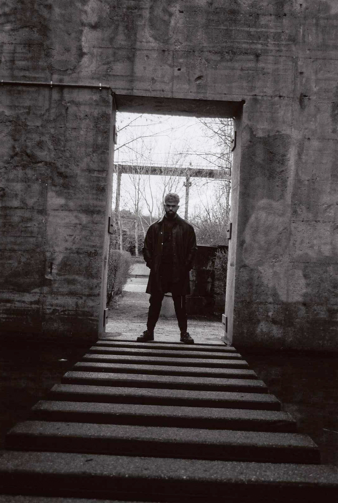 Model standing at the end of concrete steps, in a bright doorway. Location: Duisburg. Photo by NinoTurbaProductions