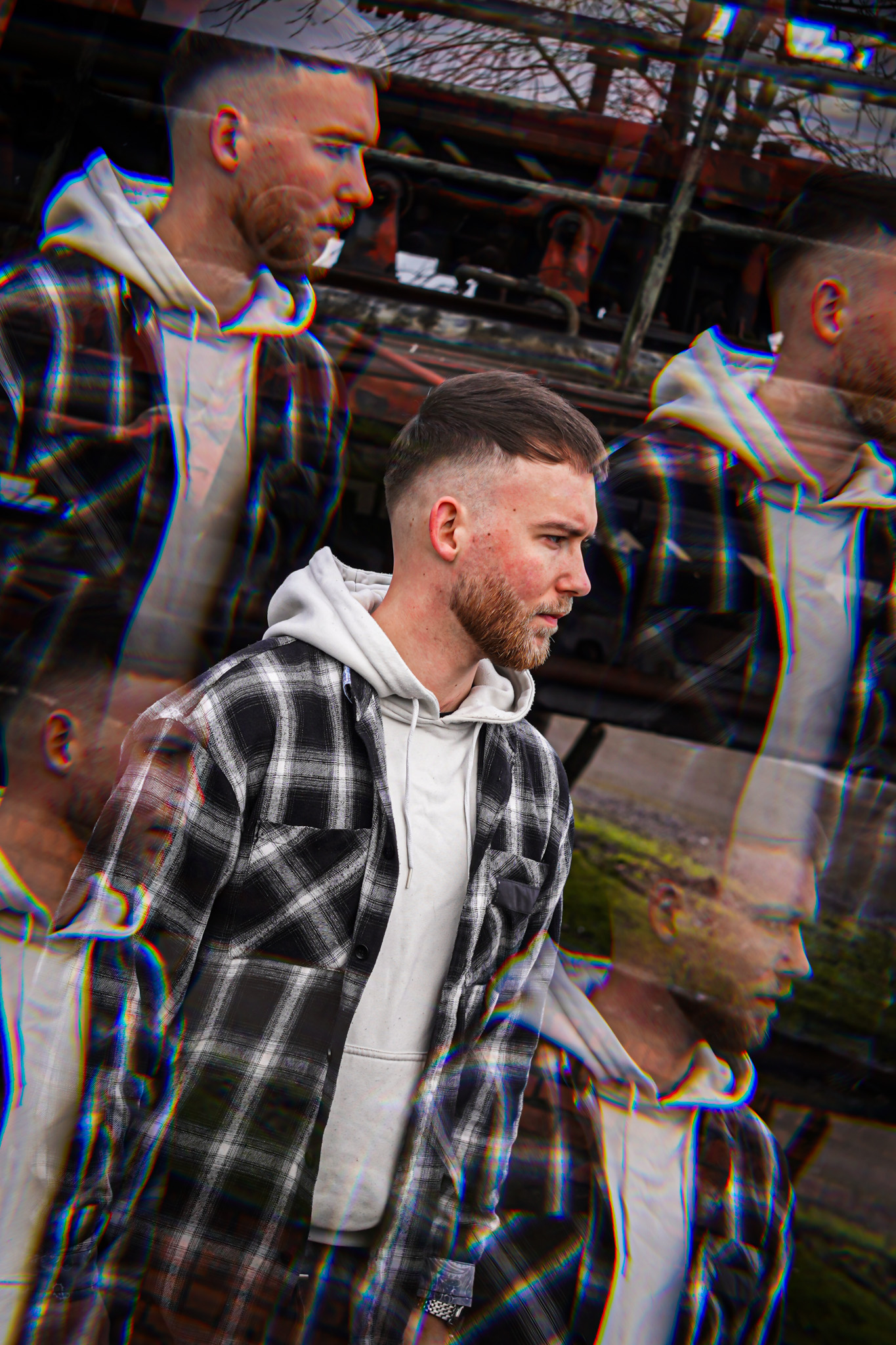 A man with a beard, seen through a repeating visual effect, wears a white hoodie and a plaid shirt. By NinoTurbaProductions