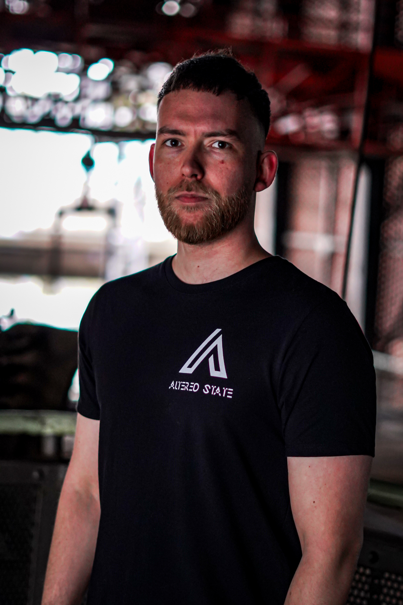 A man with a beard wears a black t-shirt with a white triangular logo and ALTERED STATE text. By NinoTurbaProductions